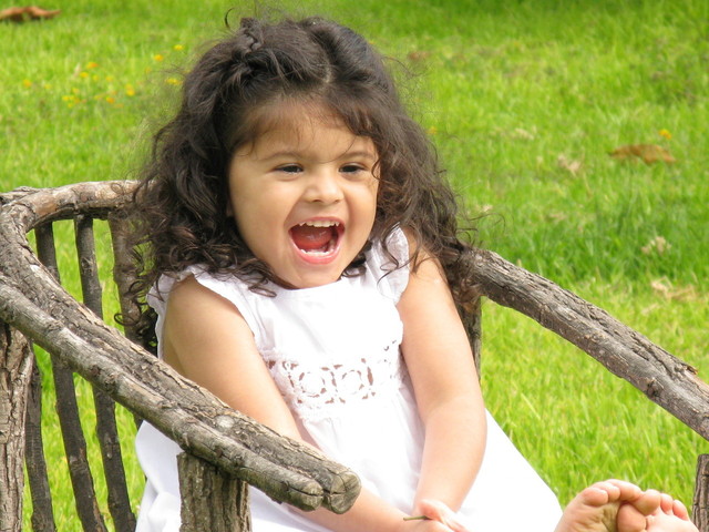 černovlasá holčička sedící v dřevěném křesílku venku